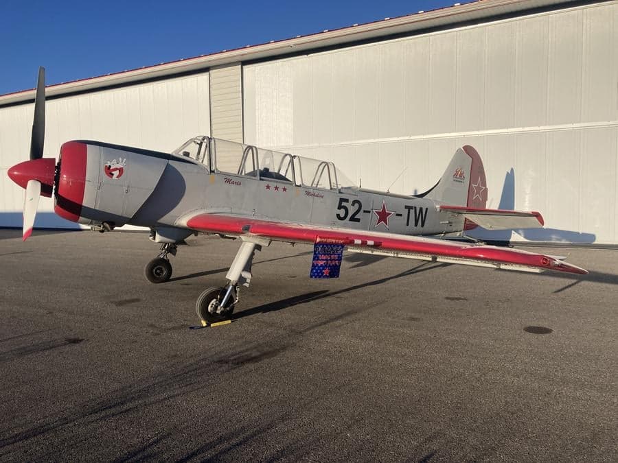Side view of a gray and red Yak-52TW aircraft on the ground.