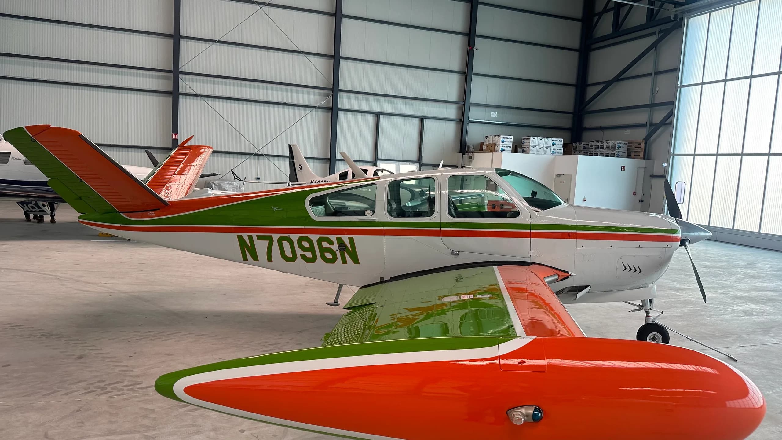 A white single-engine aircraft with green and orange stripes, registration N7096N, parked inside a hangar.