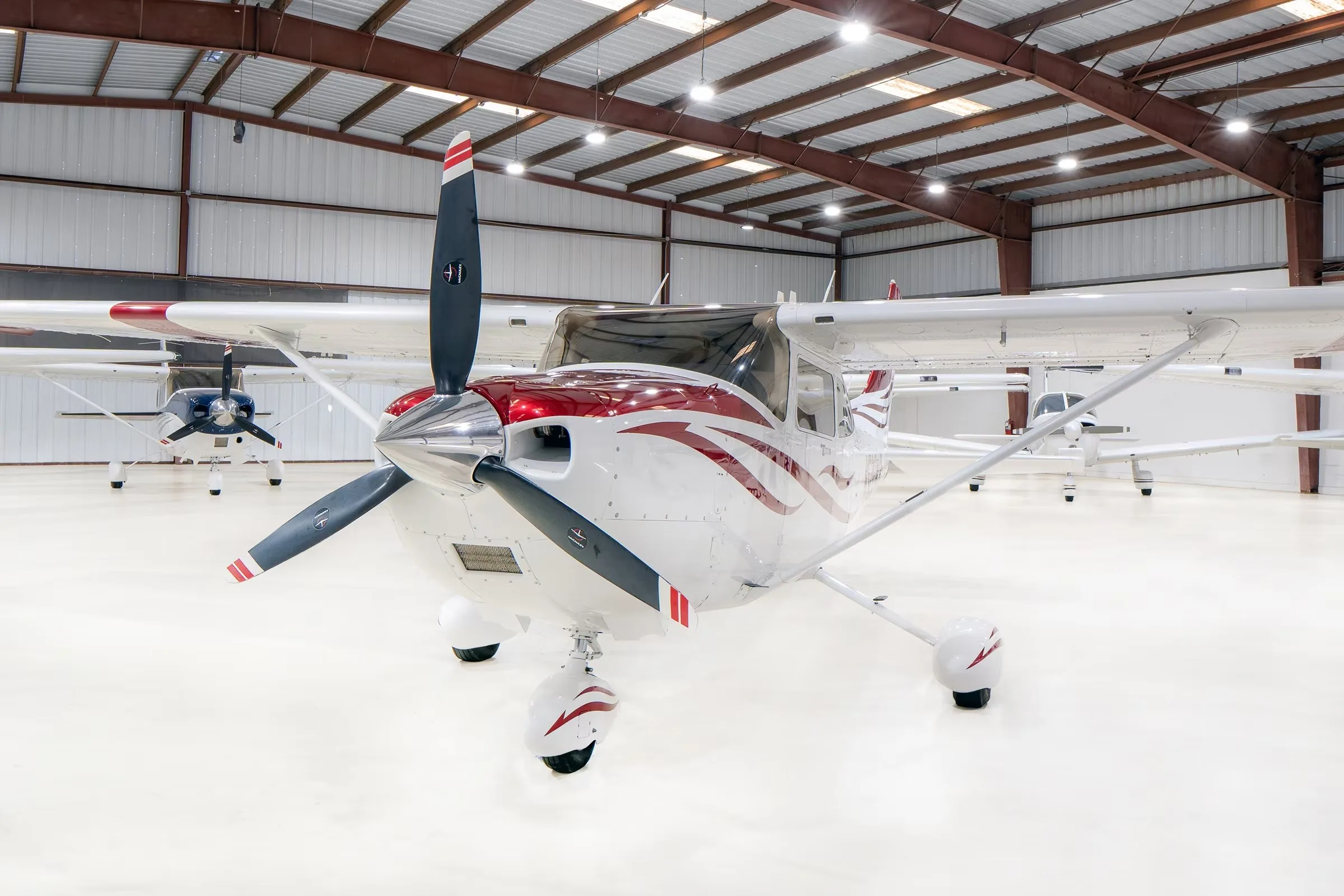 A white Cessna Skylane N520WB with red and grey stripes, parked in a hangar, viewed from the front.
