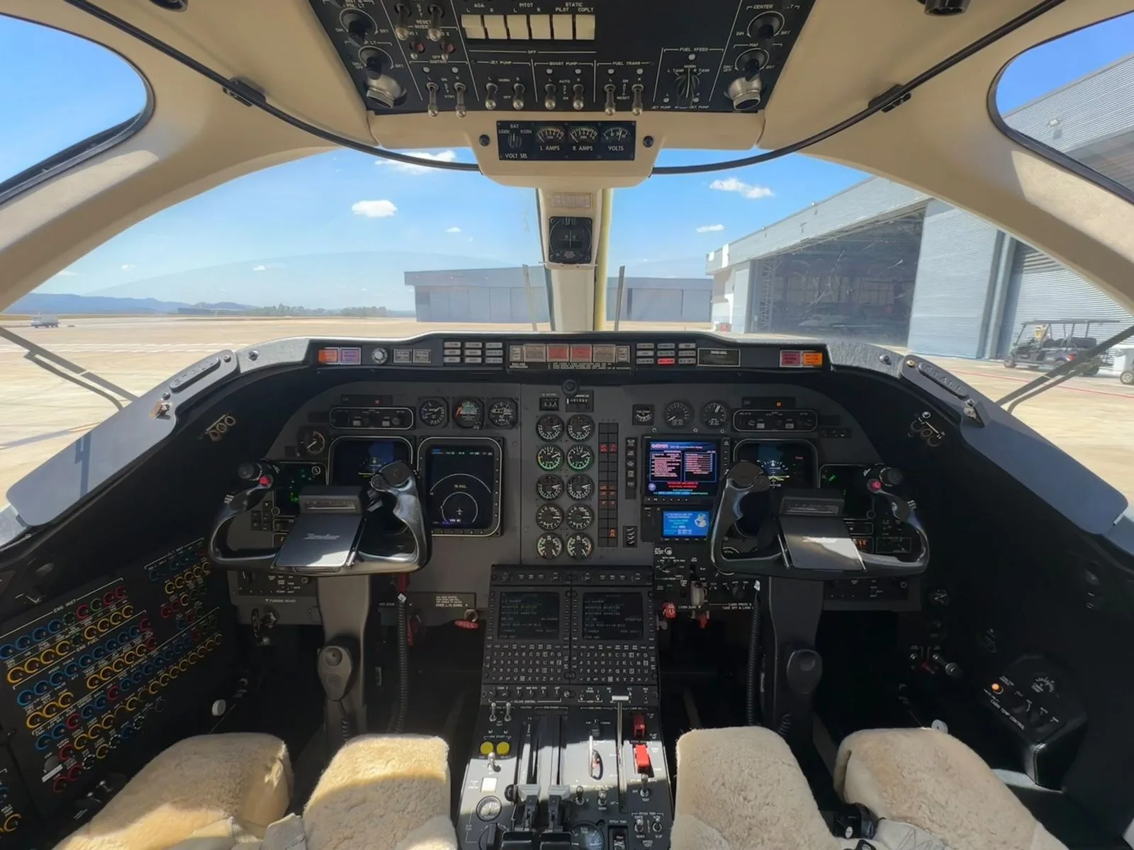 The aircraft's cockpit features a complex instrument panel with multiple screens, controls, and a clear view of the tarmac outside.