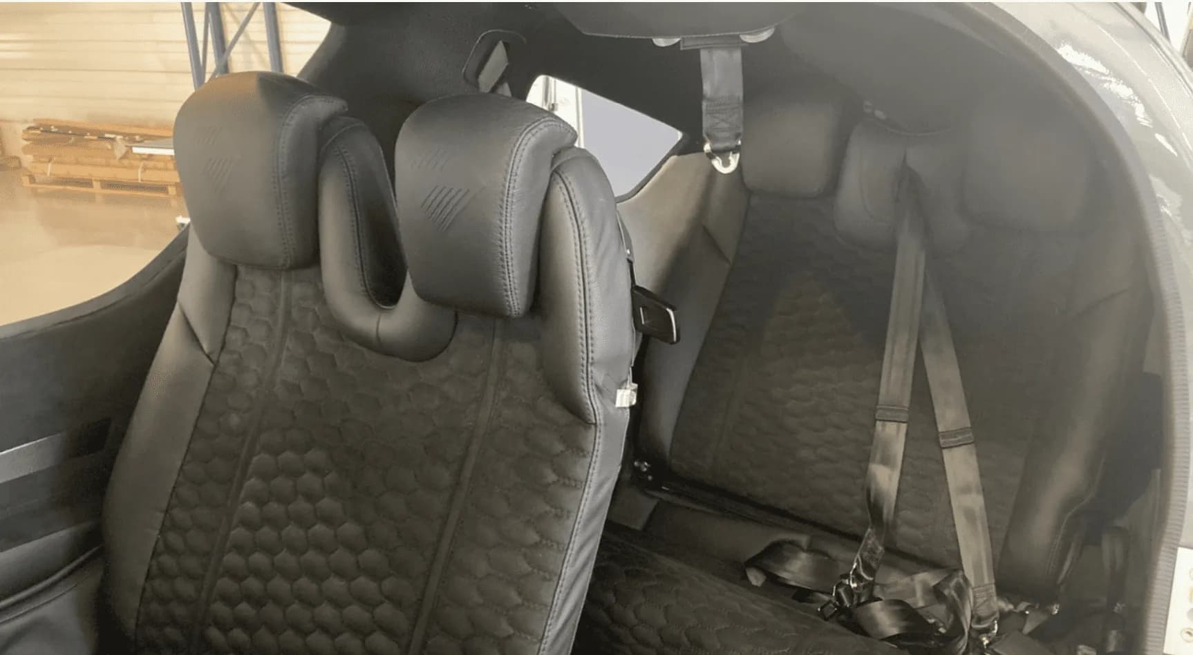 The black leather interior seats of an aircraft cabin with honeycomb pattern stitching.
