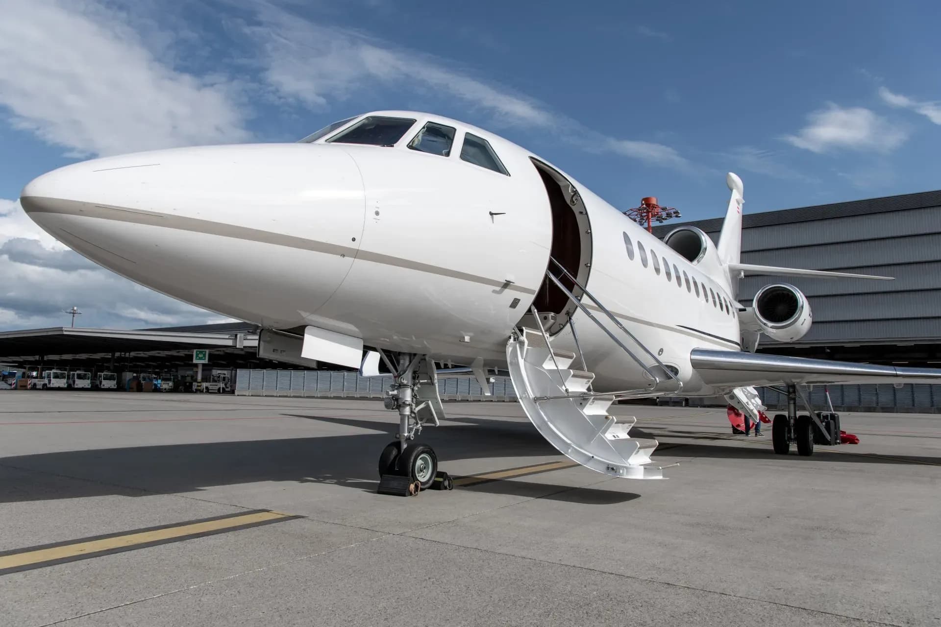 A white business jet with its main door open and stairs extended, parked on an airport tarmac under a blue sky.