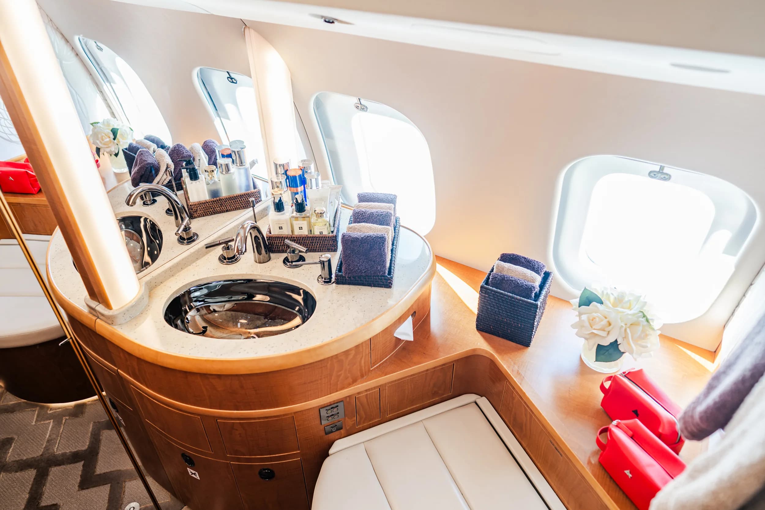 A luxurious private jet lavatory with a polished sink, mirrors, and neatly arranged toiletries.
