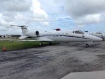 Side view of a white Learjet on the tarmac under a cloudy sky.