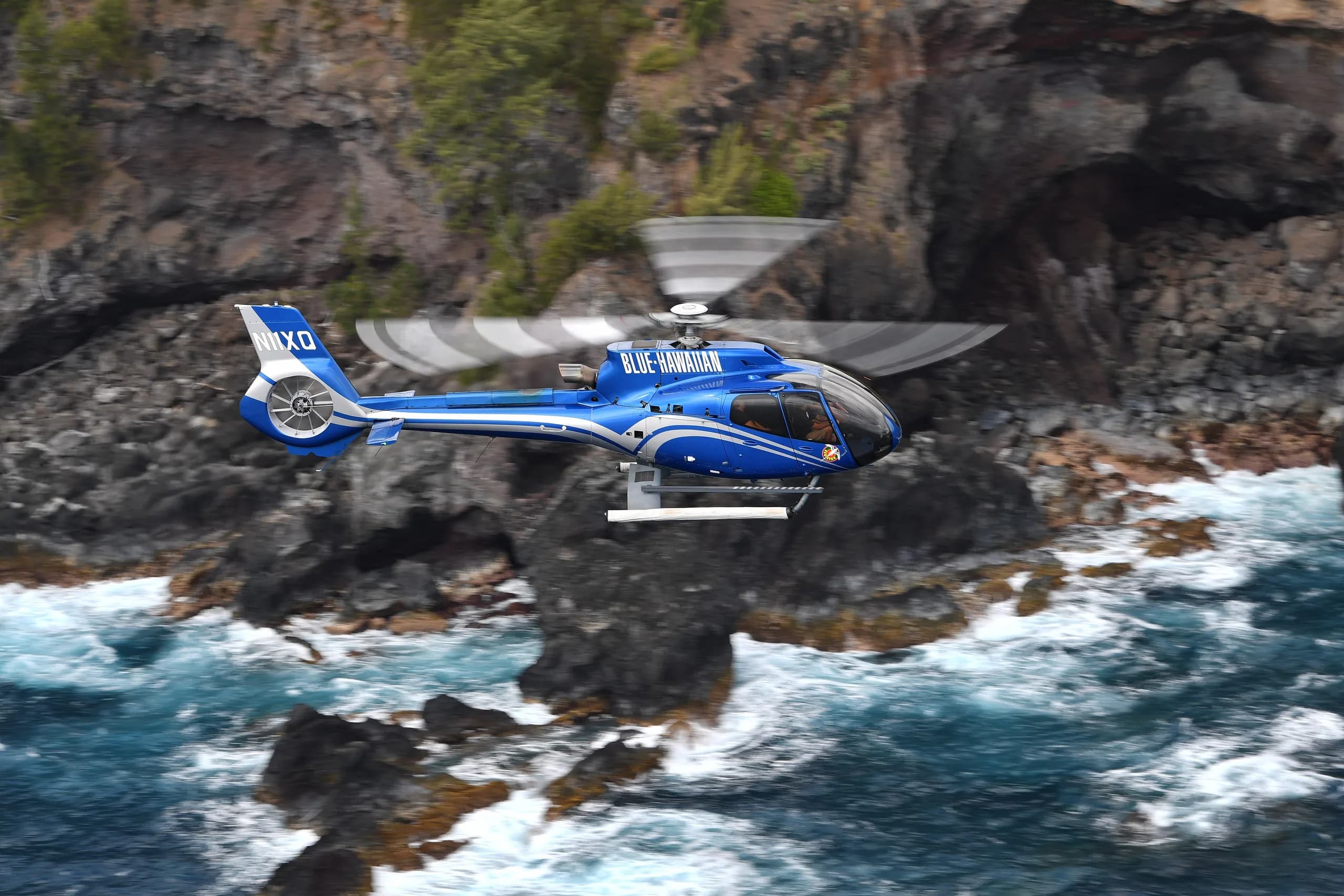 Blue Eurocopter EC135 flying near the ocean and rocks.