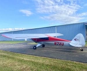 Side view of the red and silver Carbon Cub N7XU on the tarmac.