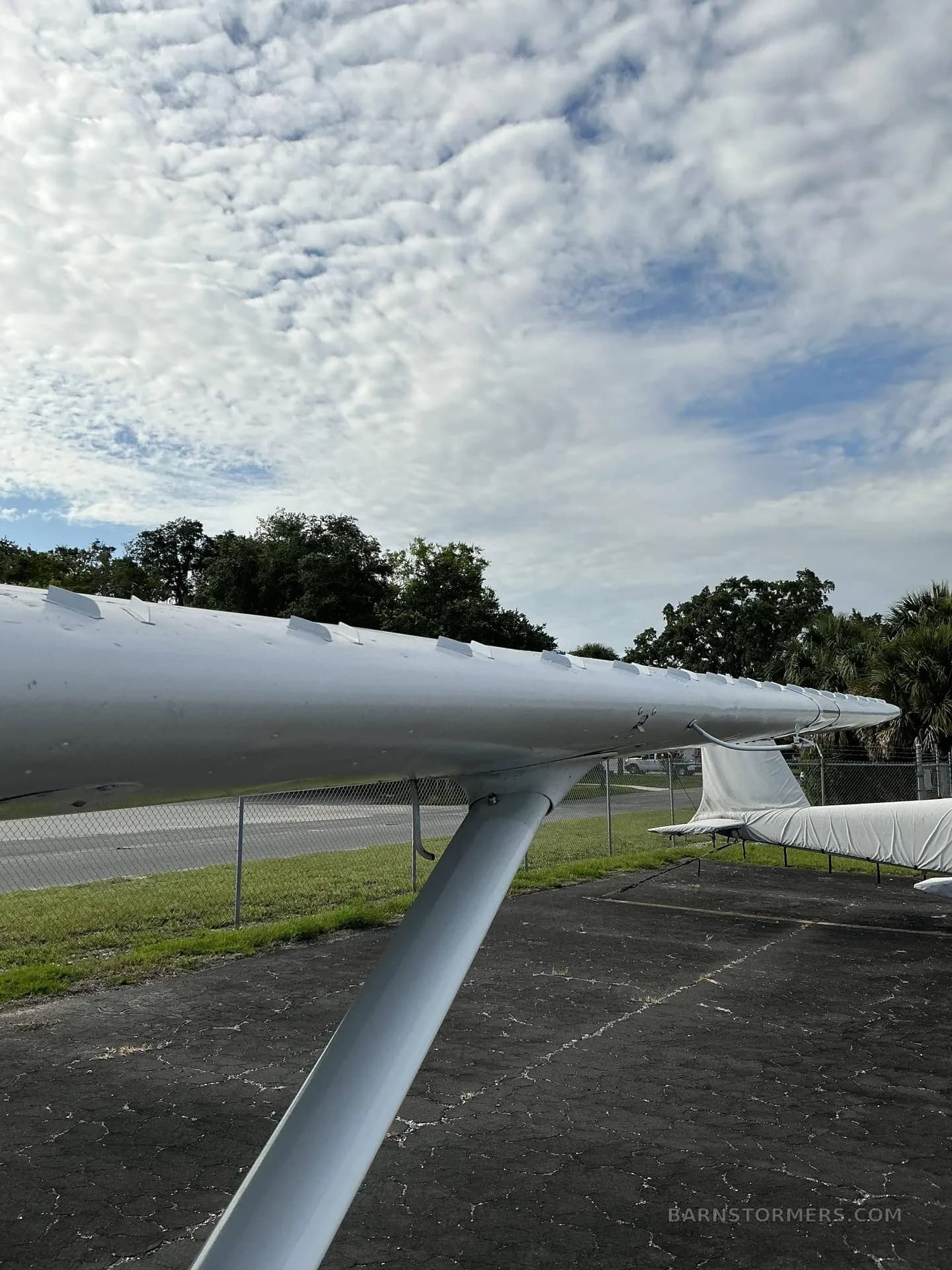 A close-up view of the white wing and fuselage of a parked aircraft against a cloudy sky.