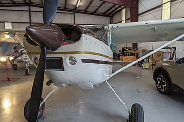 Close-up of the front of an aircraft with a brown propeller inside a hangar.