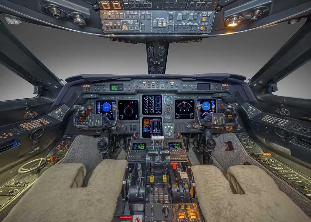 The cockpit of a private jet shows a complex array of digital displays, instruments, and controls.
