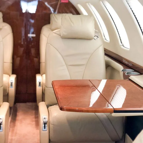 A light beige leather cabin seat with a polished wood fold-out table deployed.