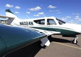 A white and green Commander 114B aircraft is parked on the tarmac.