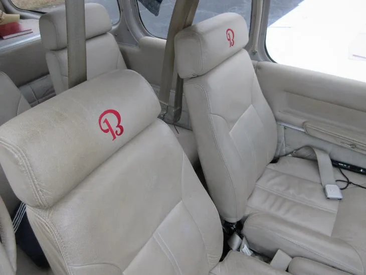 Two beige leather aircraft cabin seats with a red "B" logo embroidered on the headrests.