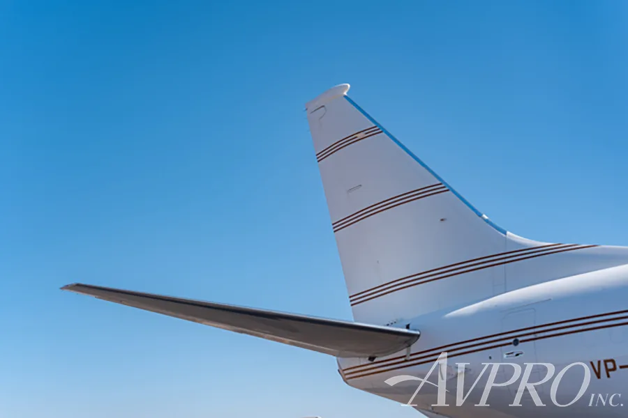 A close-up view of the white tail and horizontal stabilizer of a Boeing 737 business jet with brown stripes.