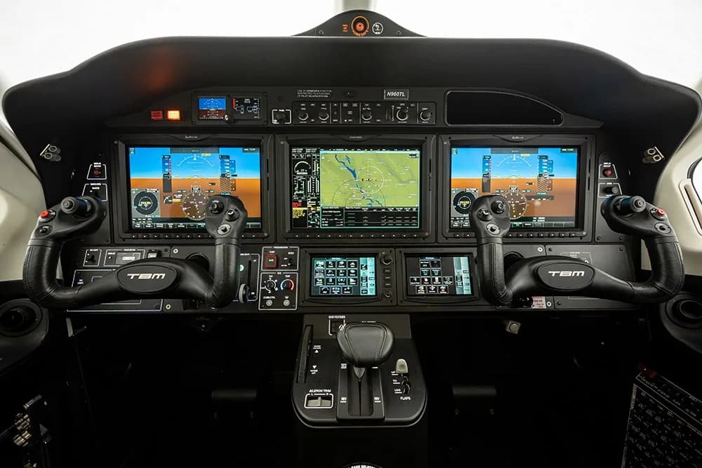 The modern glass cockpit of the TBM 960 aircraft, featuring multiple large display screens and controls.