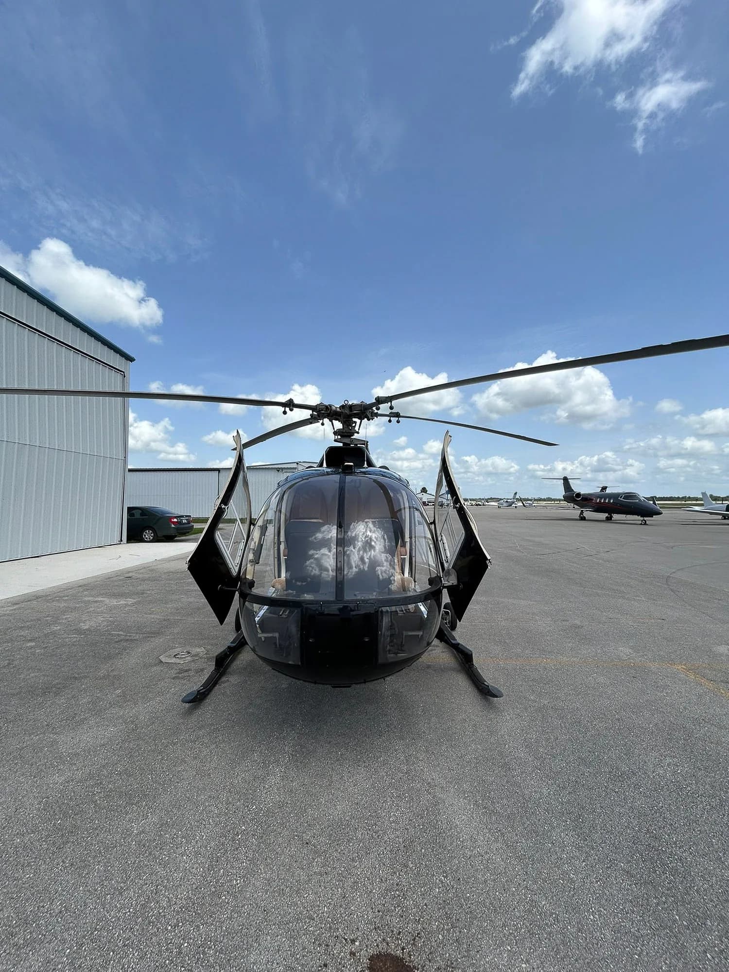 Front view of a black helicopter with open doors on the tarmac.