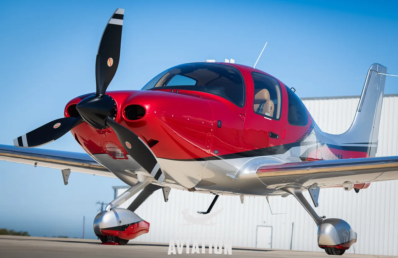 A front-quarter view of a red and silver Cirrus SR22T GTS aircraft parked on an tarmac.