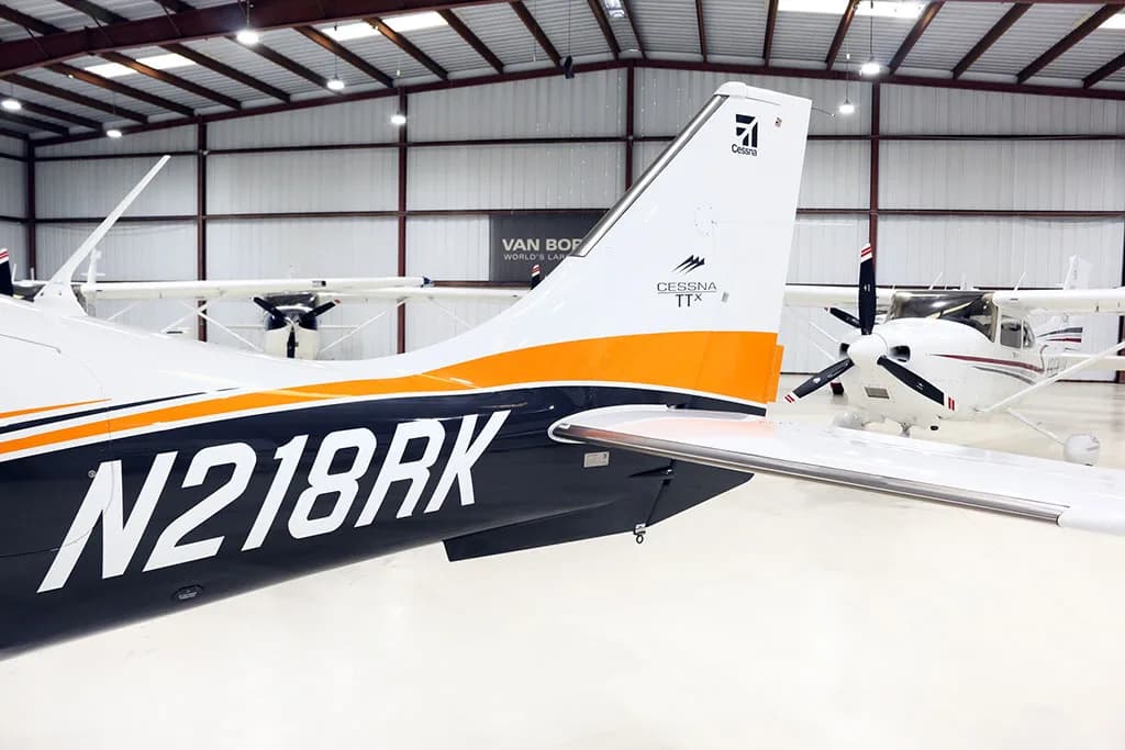 Close-up of the tail of a white, black, and orange Cessna TTX aircraft with registration N218RK, inside a hangar.