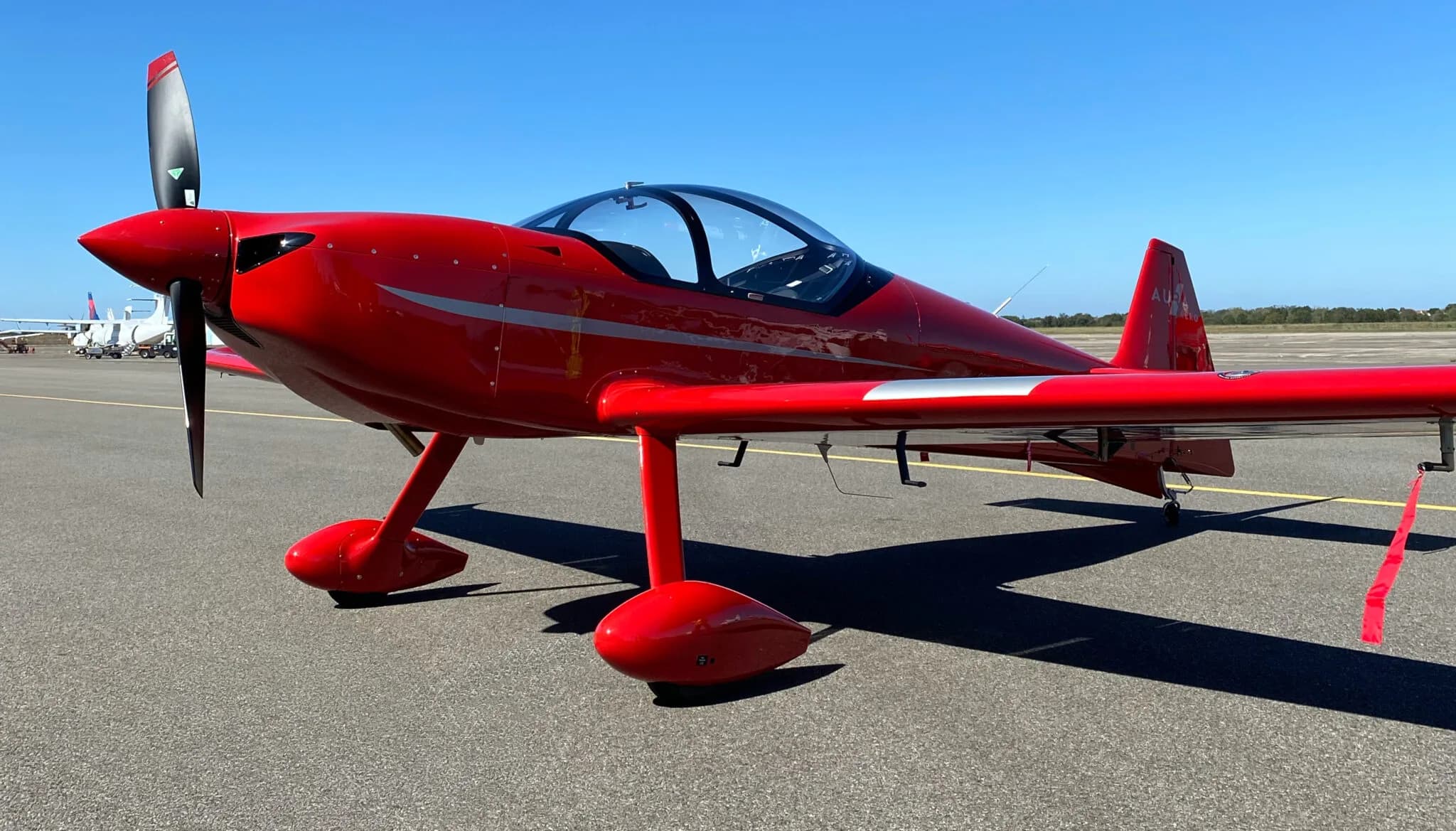 A bright red single-engine aircraft with a bubble canopy and silver stripes parked on an airfield.