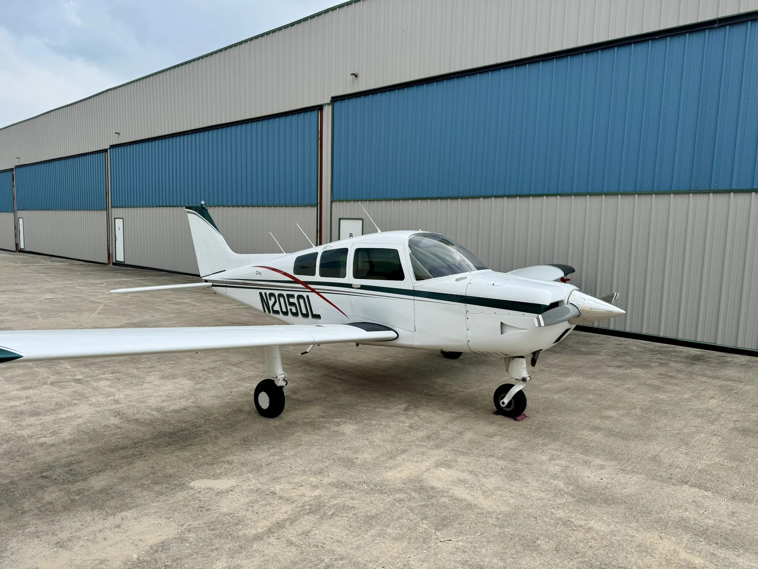 A white and green Beechcraft Sundowner N2050L parked on concrete next to a hangar.