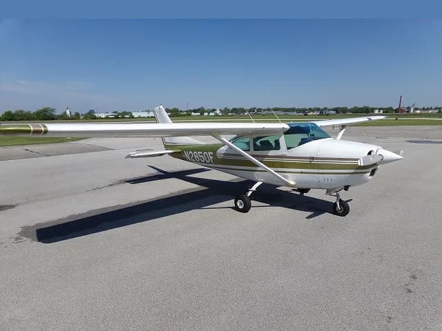 A side view of a white Cessna 182 with olive green and brown stripes, registration N2850F, parked on an asphalt tarmac.