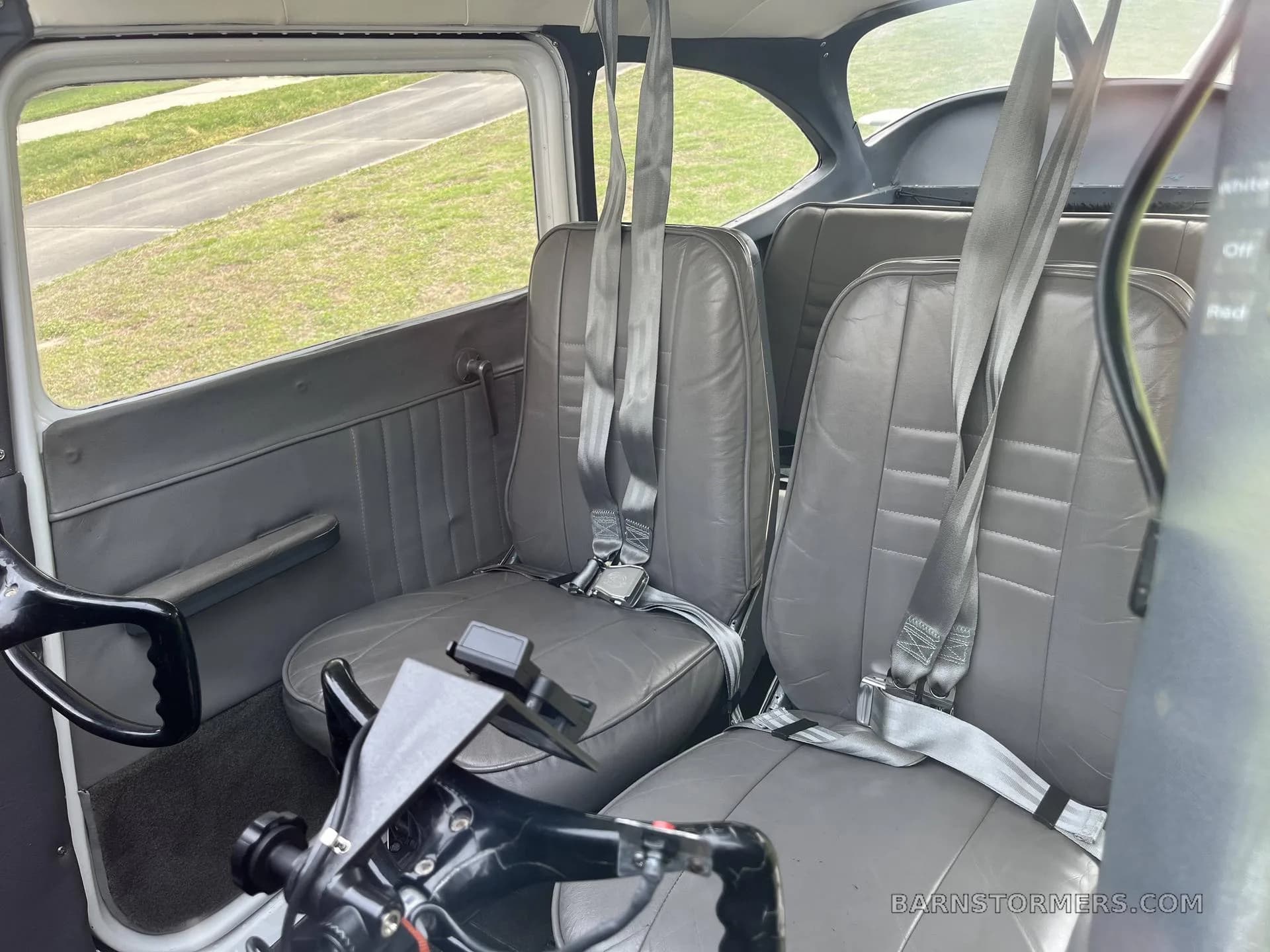 The gray interior cabin of a small aircraft shows two front seats with seatbelts and two rear seats.