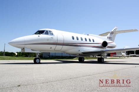 A white Hawker 800XP business jet with a dark stripe, registration N18CC, parked on an airport tarmac under a clear blue sky.