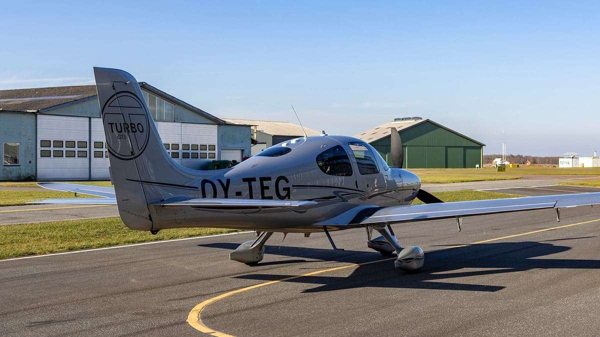 Rear side view of the silver Cirrus OY-TEG on the tarmac.