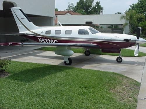 A maroon and white aircraft, N5326C, parked on a driveway with grass.