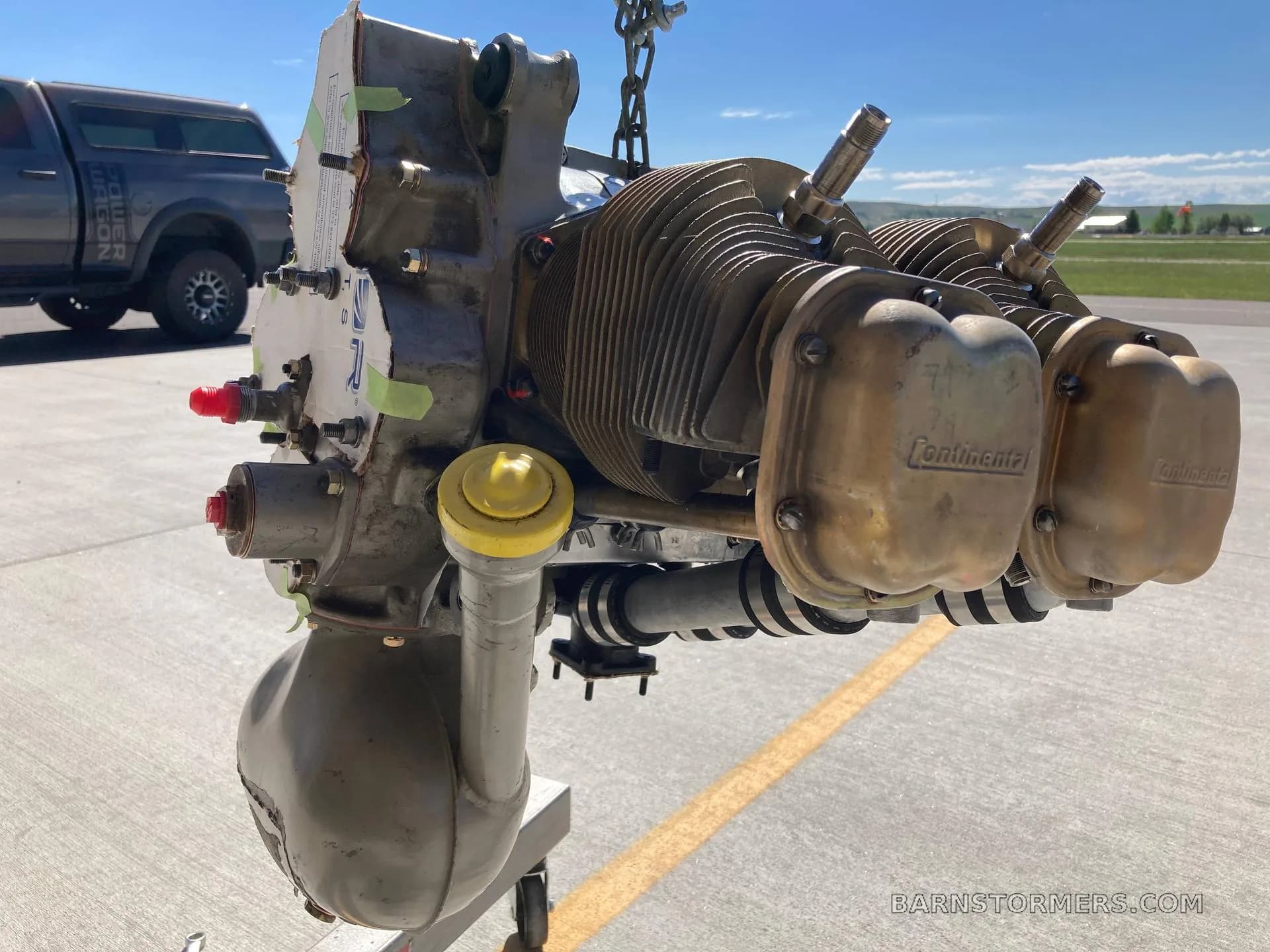 A Continental aircraft engine suspended by chains on an airfield tarmac.