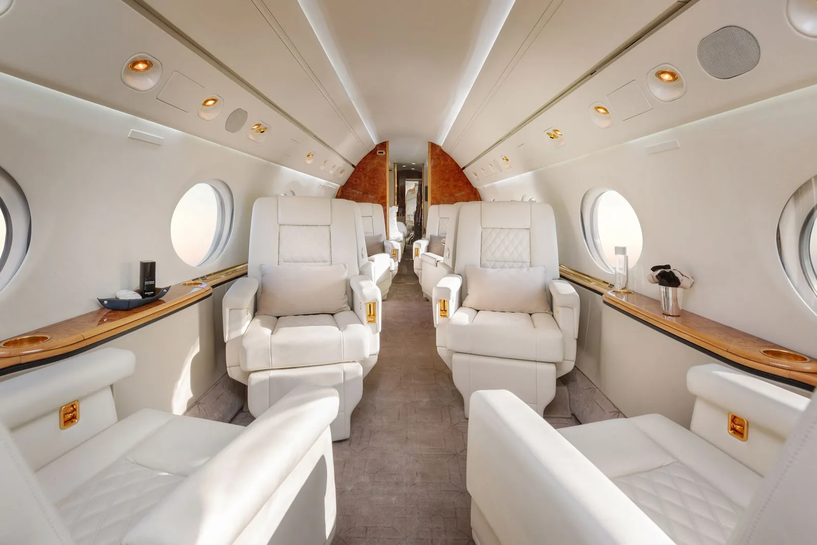 A view down the aisle of a luxurious aircraft cabin with white leather seats and wood accents.