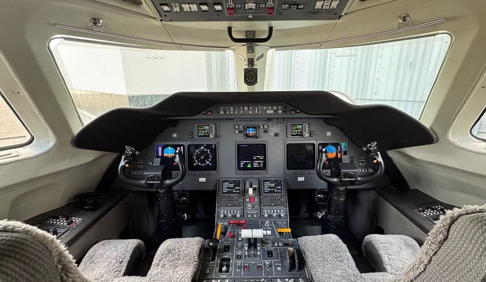 The cockpit of a business jet, showing the instrument panel with multiple displays and control yokes.