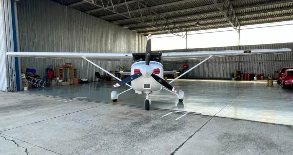 Front view of a Cessna aircraft parked inside a hangar, showing its white paint scheme and propeller.