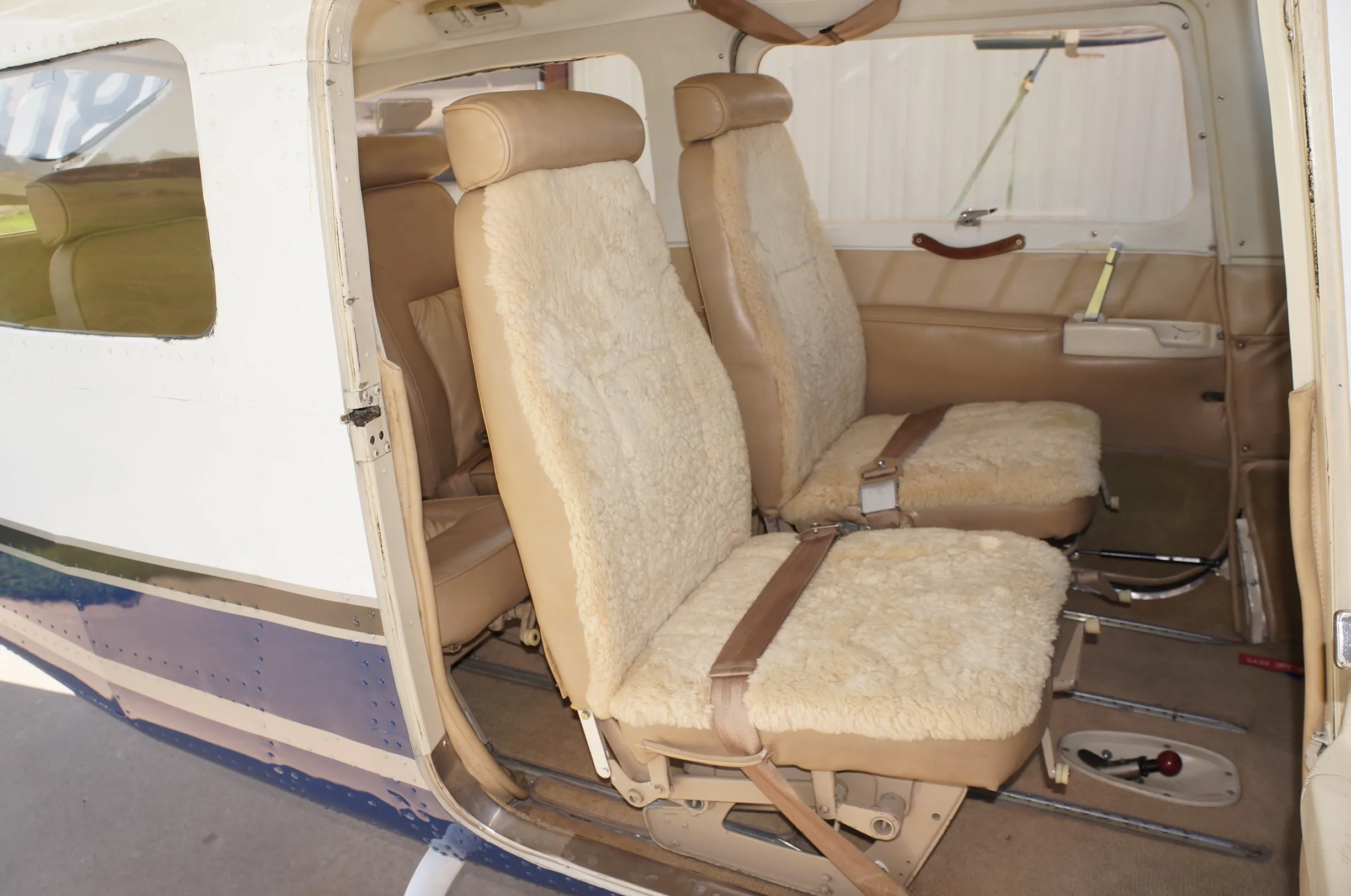 The tan sheepskin-covered front passenger and pilot seats of a small aircraft cabin, viewed from the open door.