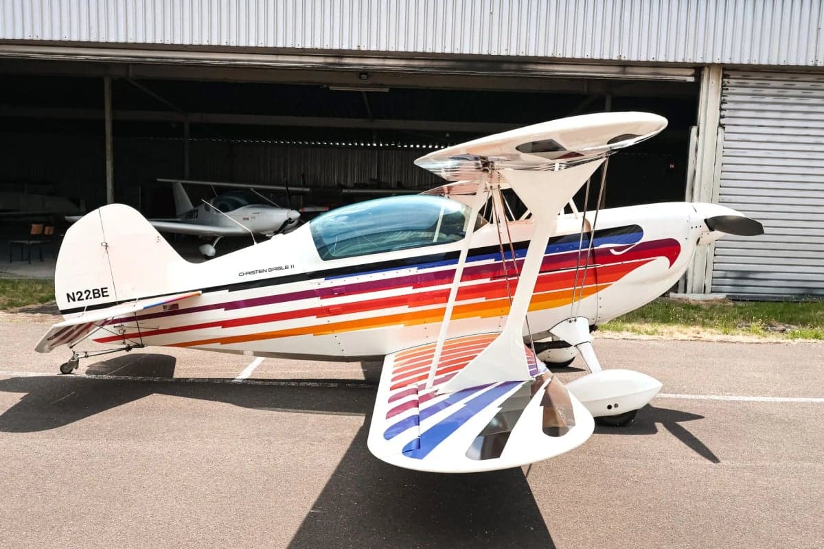 Christen Eagle II biplane with colorful paint scheme parked in front of a hangar.