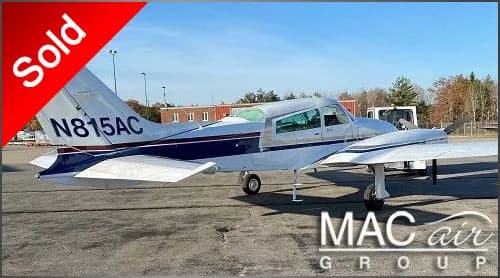 A white and blue single-engine propeller aircraft, N815AC, is parked on a tarmac under a clear sky.