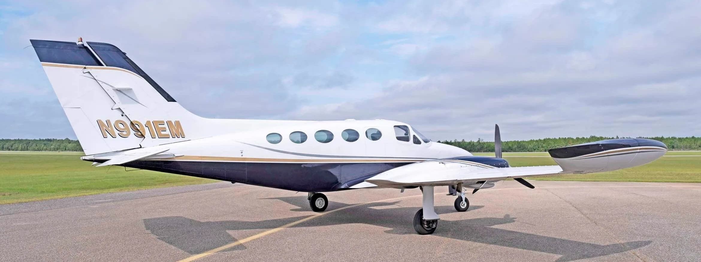 A rear-quarter view of the white and dark blue Cessna 414 Chancellor, registration N991EM, parked on an airfield.