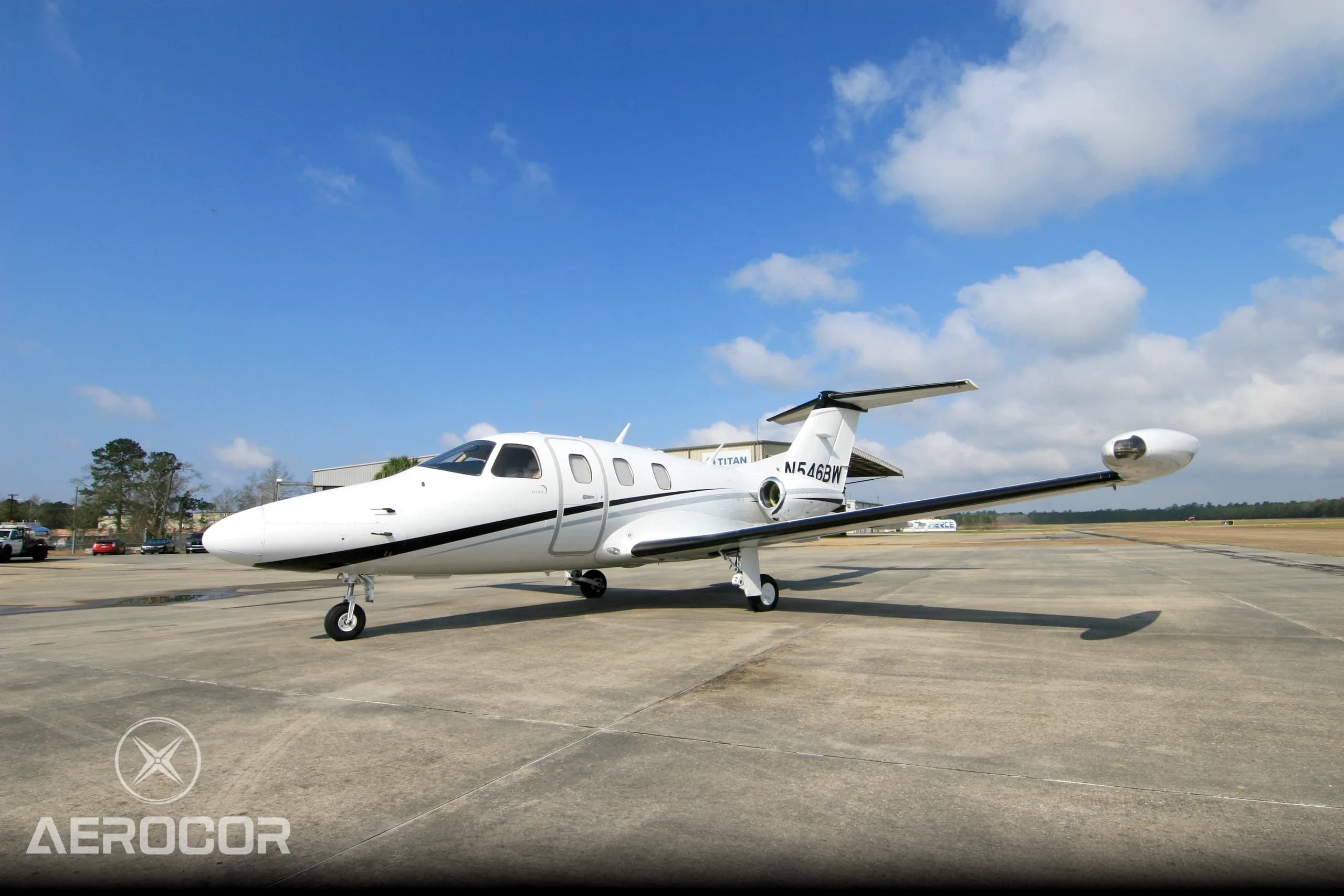 A white Eclipse 500 jet with black and grey stripes parked on an airfield under a blue sky.