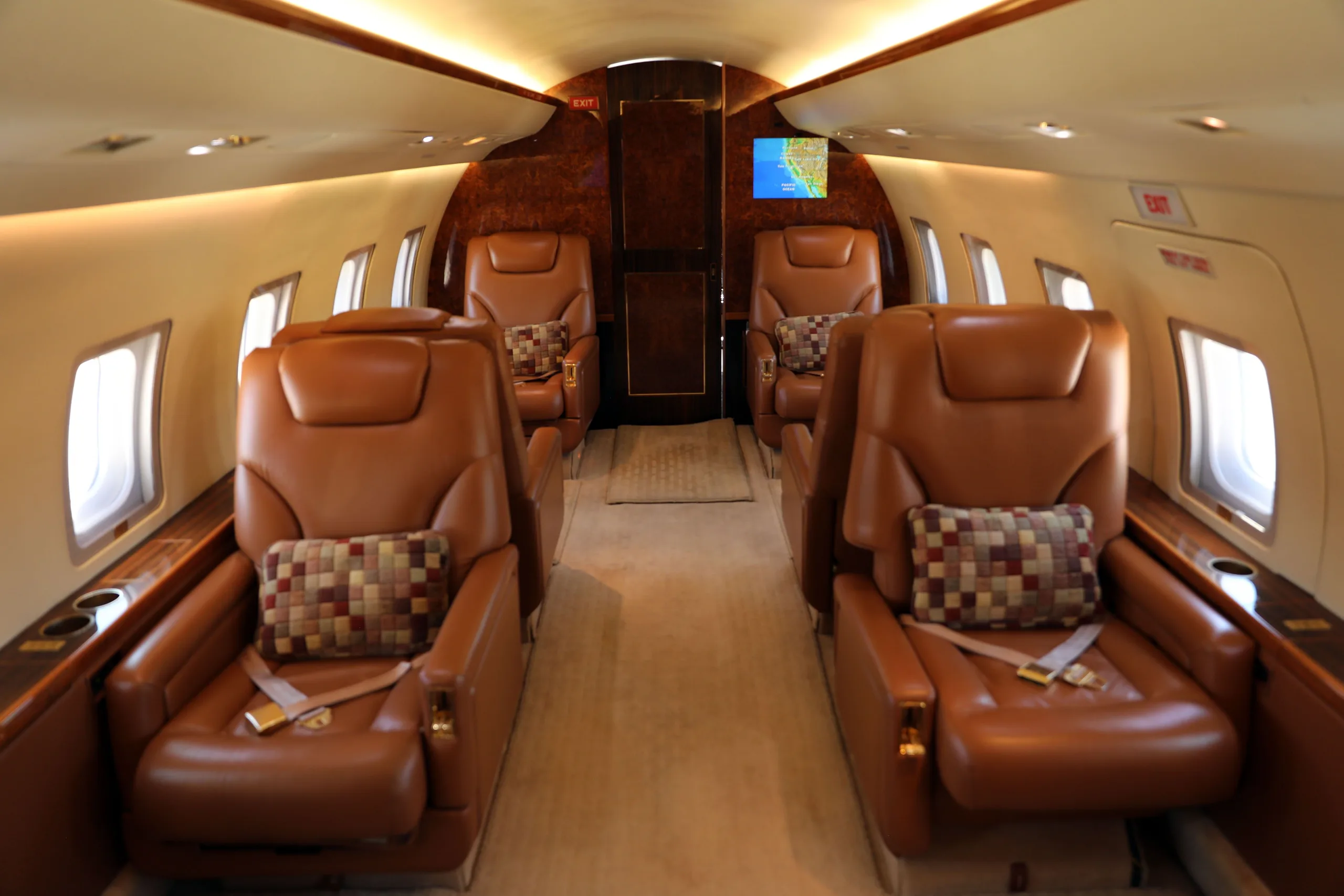 A wide view of the aircraft's cabin interior with brown leather seats and a rear monitor displaying a map.