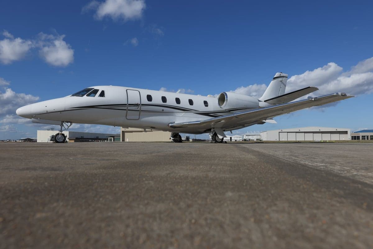 A Citation CJ3 aircraft is parked on the tarmac in front of hangars.