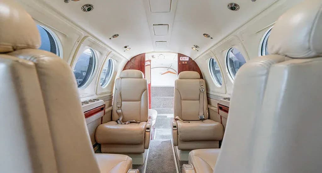 The interior cabin of an aircraft, showing beige leather seats facing each other and an exit door at the rear.