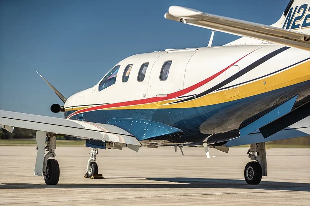 A close-up side view of the white, blue, and gold painted turboprop aircraft (N220MA) on an airfield.