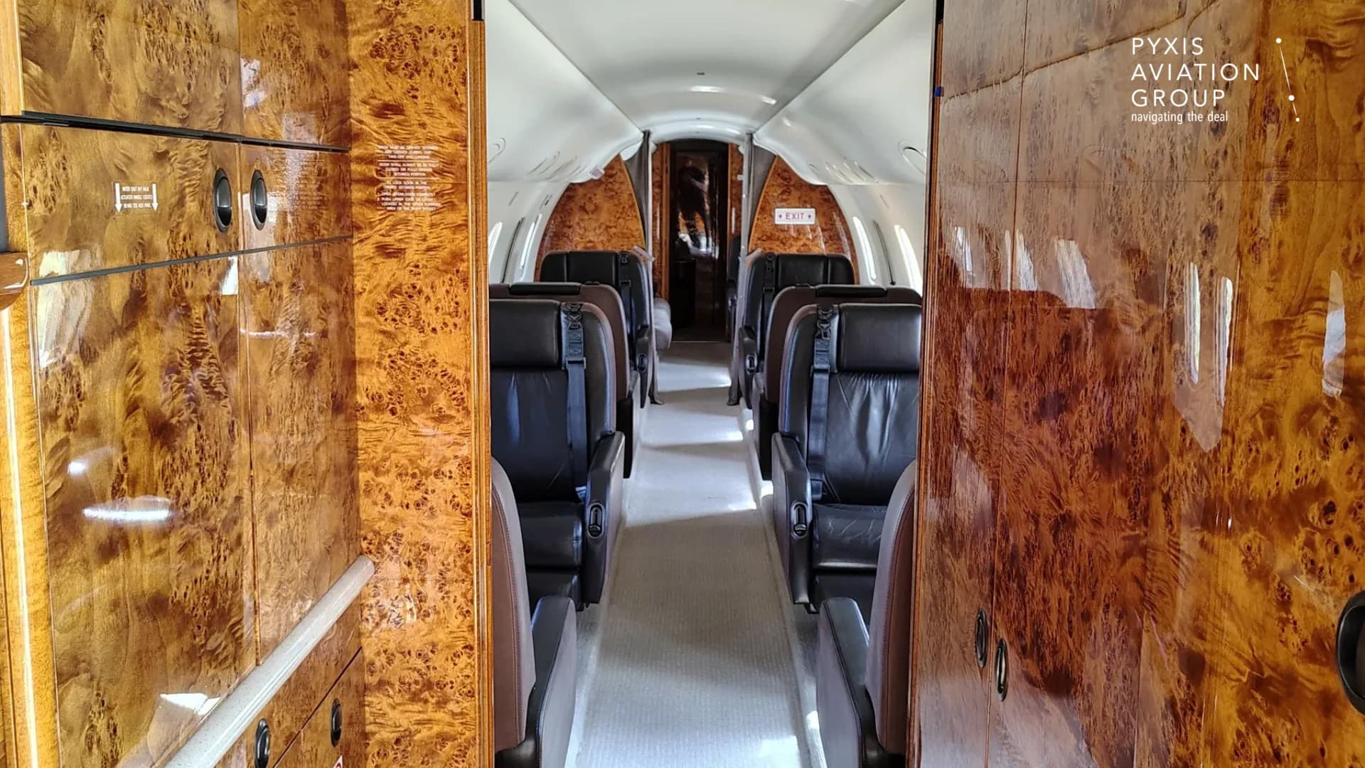 A long view down the aircraft cabin aisle, flanked by wood-paneled walls and dark leather seats.
