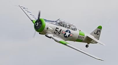 A silver and green T-6 Texan aircraft flying in the sky.