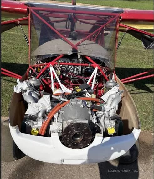 A front view of the exposed engine and internal frame of a red ultralight aircraft.