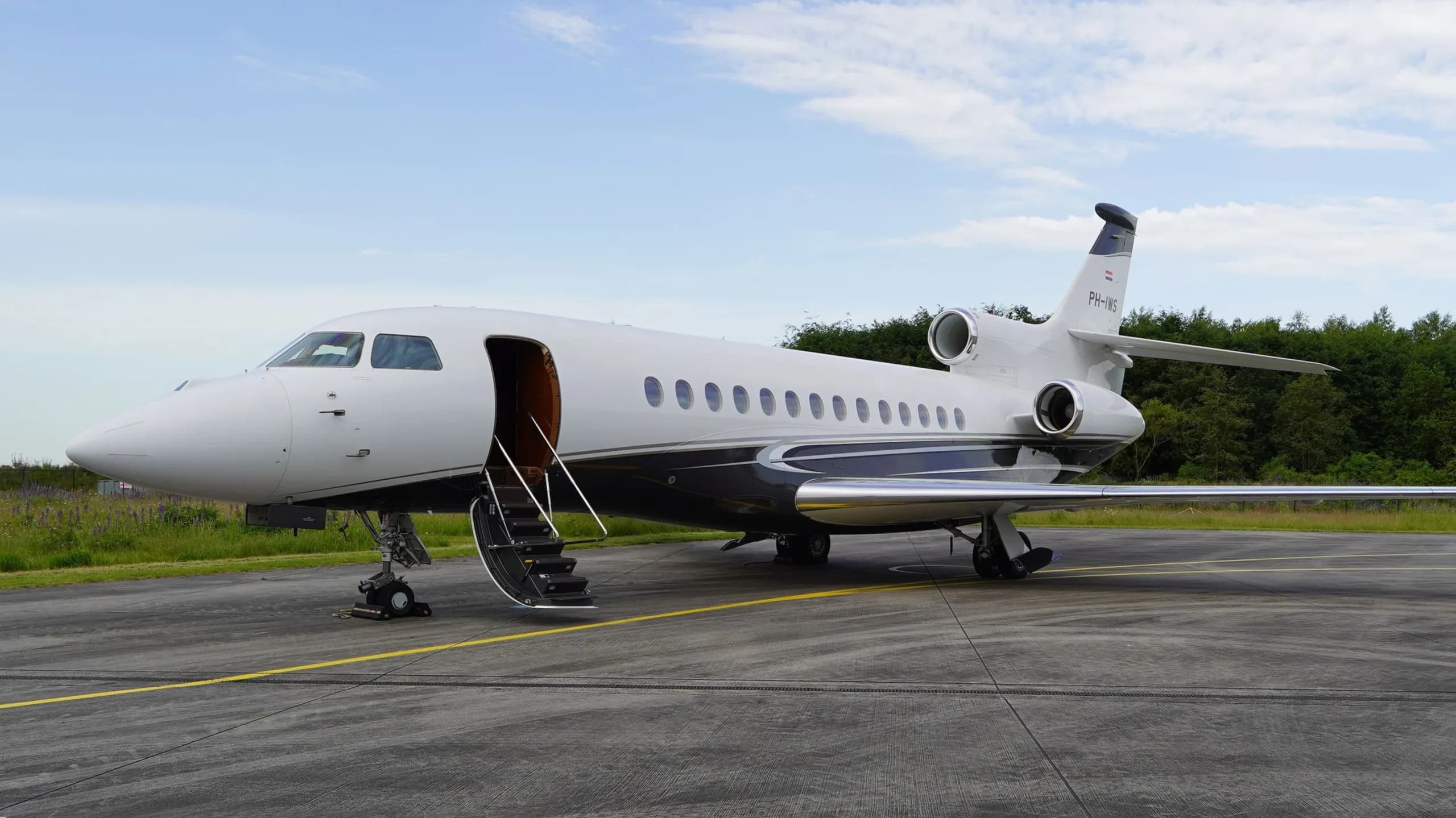 A white and dark blue Dassault Falcon business jet with its main door open and stairs extended, parked on an airfield.