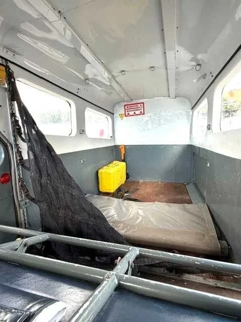 The interior cabin of an aircraft configured for cargo, showing a yellow container and a mattress on the floor.