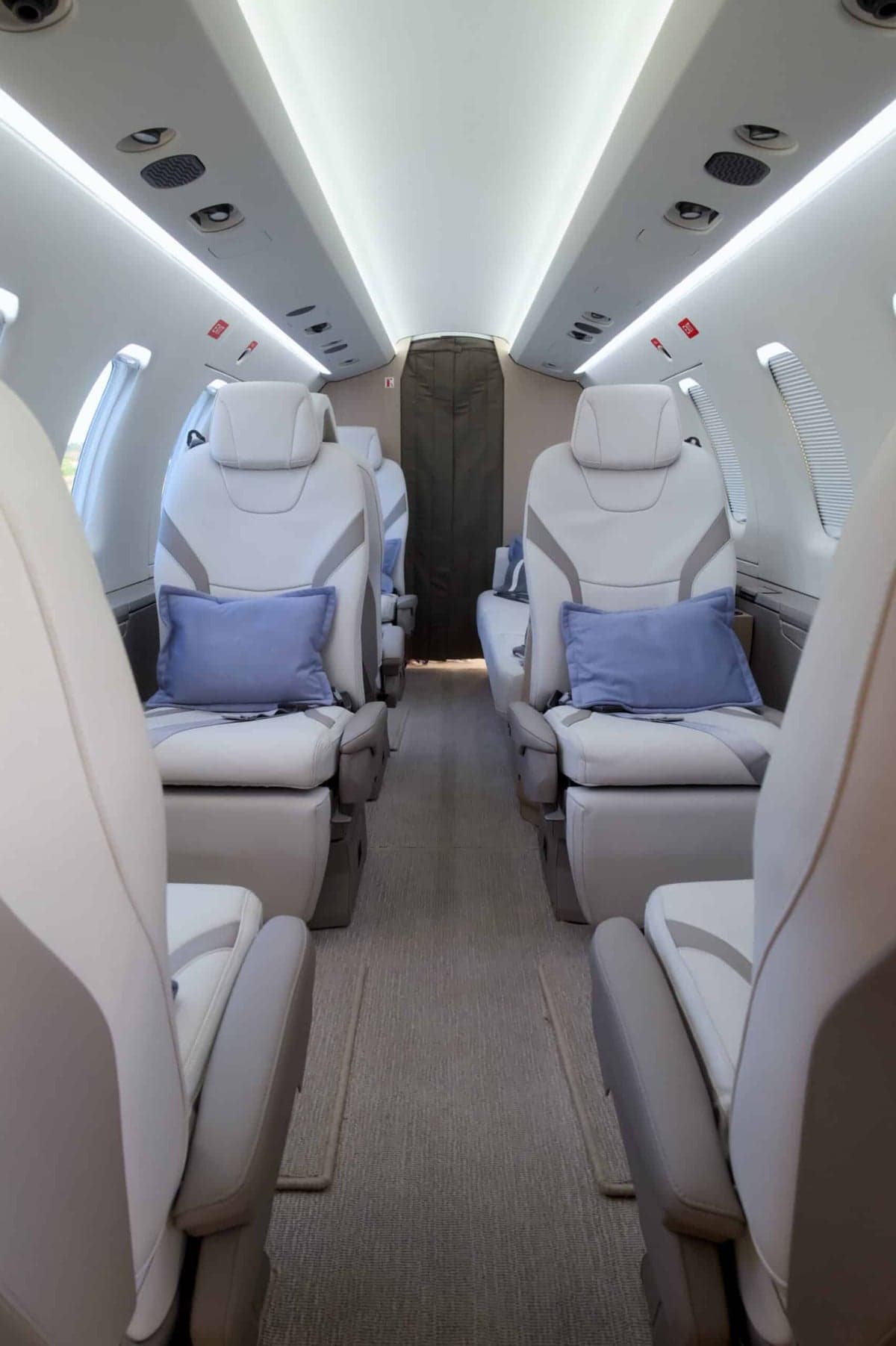 View of the aircraft's interior cabin with white leather seats and blue pillows.