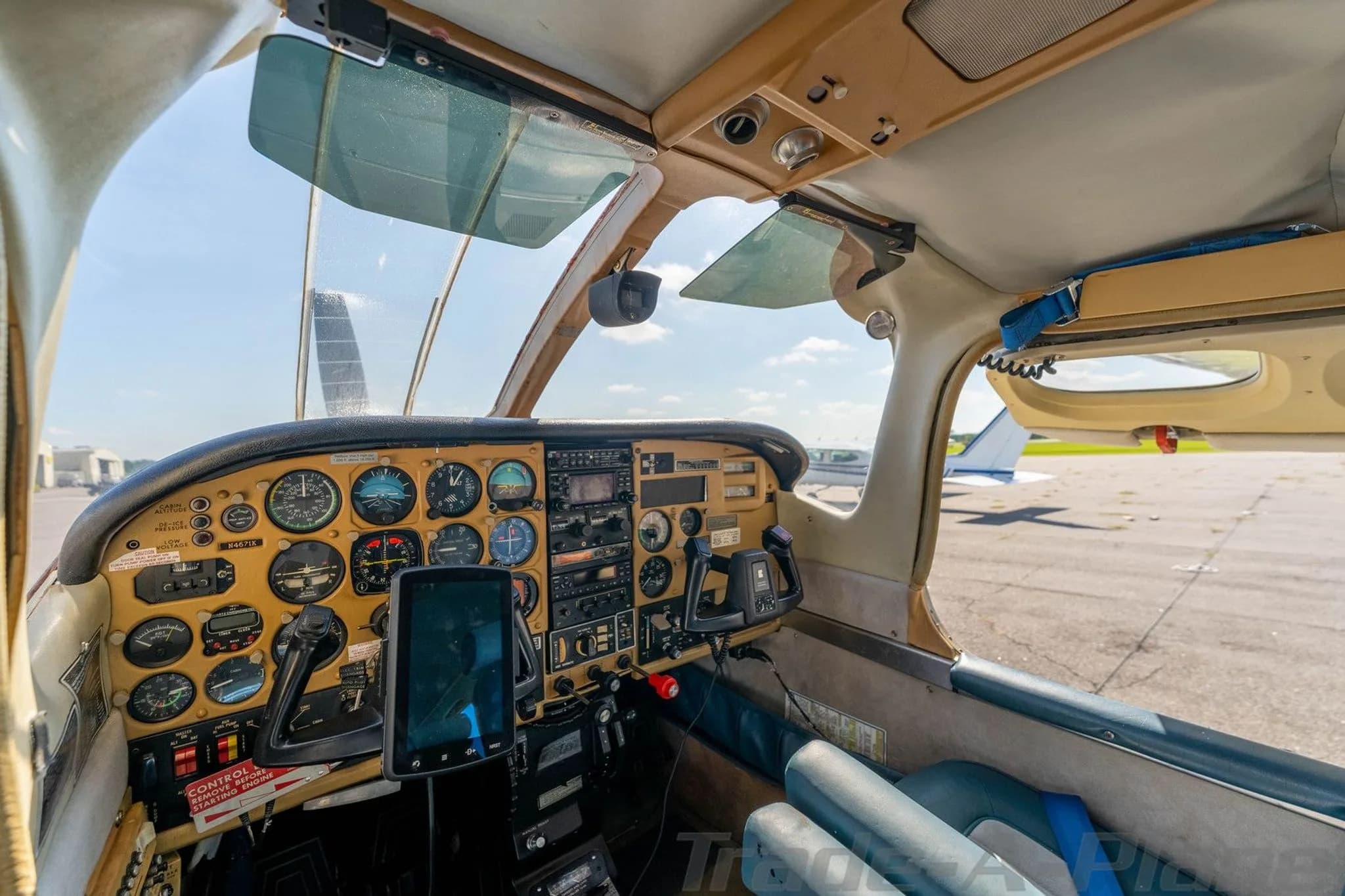 A wide view of the aircraft's cockpit, showing the instrument panel, yokes, and a view out the windshield to the tarmac.