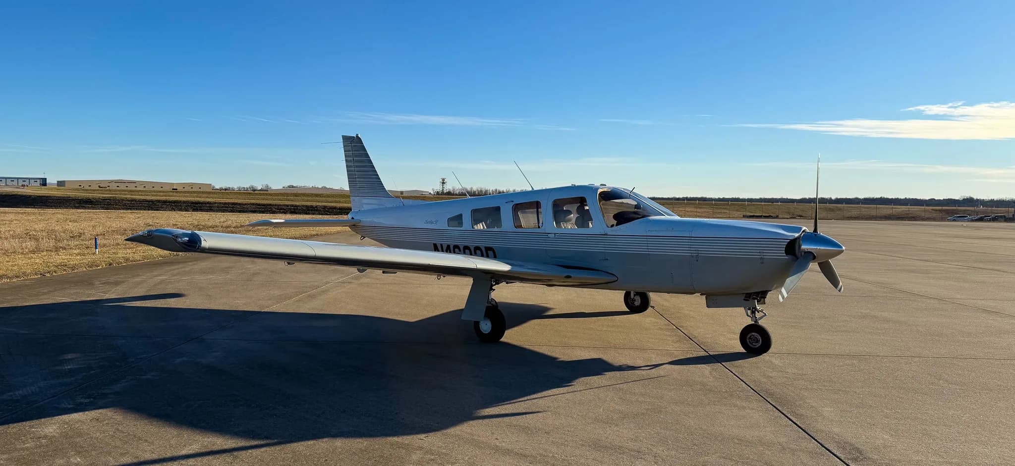 A front three-quarter view of a white Piper Saratoga SP (N1622P) with grey stripes on an airfield.