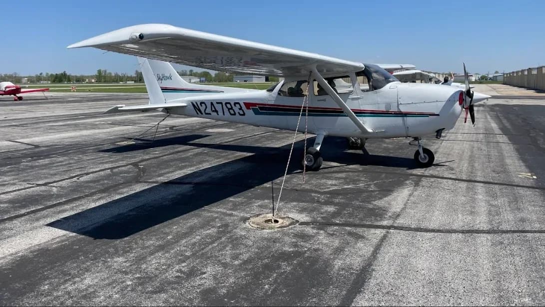 A white Cessna 172 Skyhawk, N24783, with blue and green stripes, parked and tied down on an asphalt ramp.